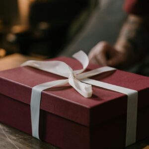 A stylish red gift box with a white ribbon on a wooden surface, perfect for special occasions.