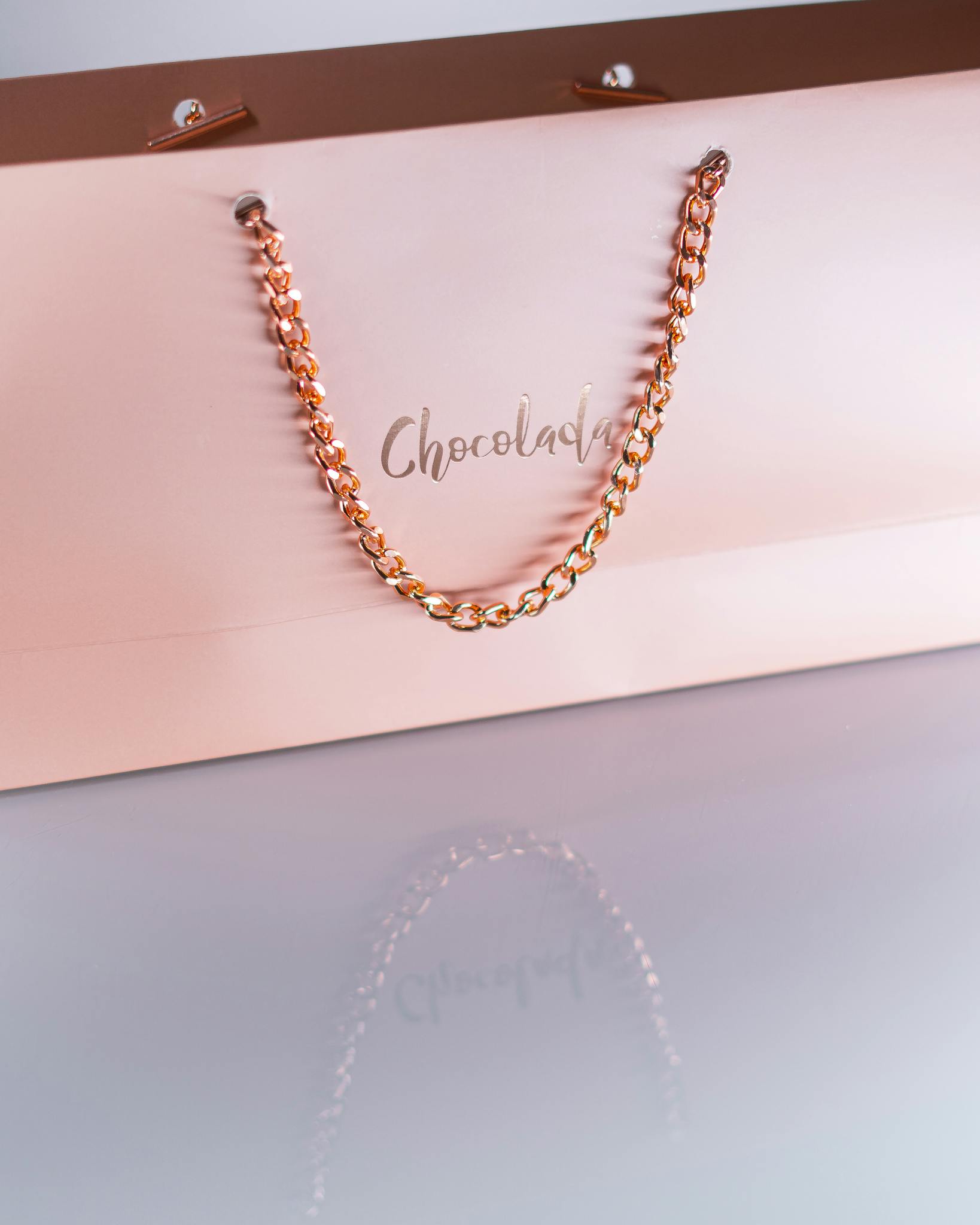 Sophisticated chocolate gift bag featuring a luxurious golden chain handle on a light background.